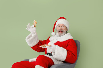 Fototapeta na wymiar Santa Claus with tasty gingerbread cookies sitting in armchair on color background