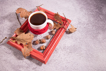 A Cup of acorn coffee in a red knitted decor and a red frame with acorns, oak leaves on a concrete...