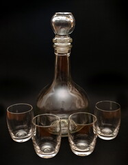 Glass transparent decanter and four glasses close up on a black background