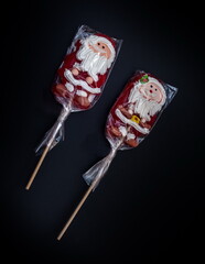 Two lollipops in the shape of Santa Claus on a stick in a transparent film closeup on a black background