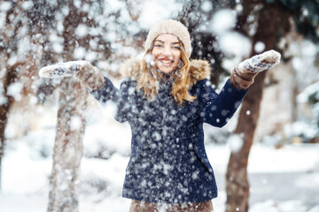 Playing with snow on winter holidays, a woman throws white, loose snow into the air. Young woman enjoying the winter weather. Christmas, New year.