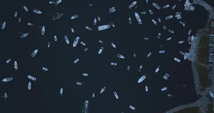 Extremely interesting, high altitude, slowly descending aerial footage of small motor boats, sail boats gathering around and witnessing the biggest bonfire event on Earth at Alesund, Norway at dusk.