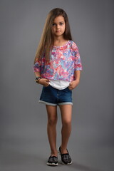 charming little girl in a motley blouse and denim shorts posing on a gray background