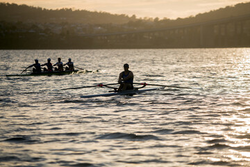 Early morning view on the river Derwent in Hobart of a a single sculler and coxless four rowers...