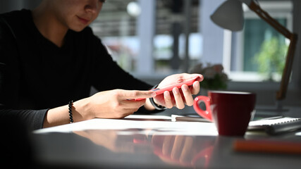 Cropped shot of man graphic designer hands holding smart phone at his workspace.