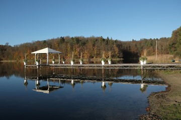 Moody landscape with wooden pier with white gazebo over a lake surrounded by forest in autumn...