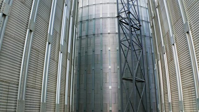 Exterior of modern plant. Large metal grain elevators outdoors. Aluminum containers for storing and processing crop. Close-up.Camera rising up.