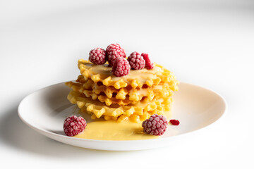 Weekend breakfast: waffles with condensed milk and raspberries. White background. Viennese waffles with condensed milk and raspberries on a white plate