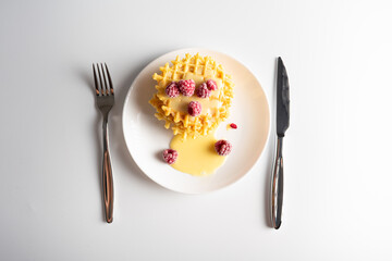 Weekend breakfast: waffles with condensed milk and raspberries. White background. Viennese waffles with condensed milk and raspberries on a white plate