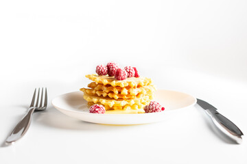 Weekend breakfast: waffles with condensed milk and raspberries. White background. Viennese waffles with condensed milk and raspberries on a white plate