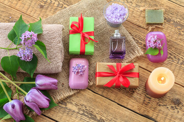 Fototapeta na wymiar Towels, soap, gifts, candle and lilac flowers on wooden background.