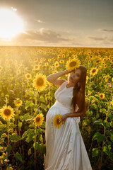 Beautiful caucasian pregnant woman walking in the summer at sunset in a field of blooming sunflower