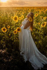 Obraz na płótnie Canvas Beautiful caucasian pregnant woman walking in the summer at sunset in a field of blooming sunflower