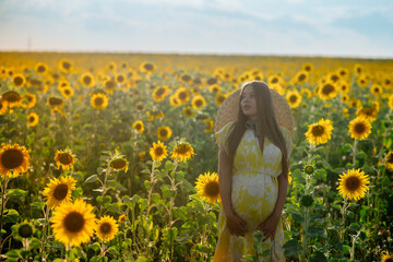 Beautiful caucasian pregnant woman walking in the summer at sunset in a field of blooming sunflower
