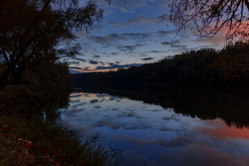 autumn landscape, nightfall and dark forest, trees near river and blue sky