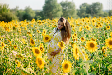 Beautiful caucasian pregnant woman walking in the summer at sunset in a field of blooming sunflower