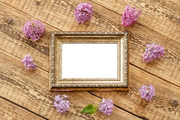 Vintage photo frame with lilac flowers on wooden background.
