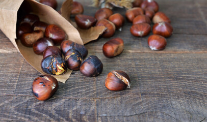 roasted chestnuts  in a papaer bag spilled on wooden table