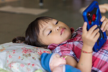 Obraz premium Selective focus. Portrait​ image​ of​ 2-3​ years​ old​ baby.​ Happy​ Asian​ child​ girl​ using and​ playing​ a​ smart Phone.​ She laying on the bed.