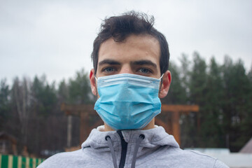 A cute guy with beautiful blue eyes wearing a mask on the street. Protection against viruses and coronavirus