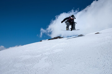Young woman on a snowboard makes a flight after jumping from a snowy ledge against a dark blue sky high in the mountains in winter