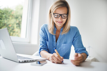 young and blond business woman with blue shirt and glasses is working in office and is happy