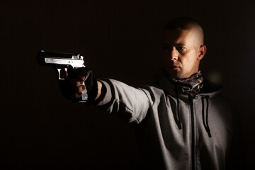 Fototapeta na wymiar Determined man with short haircut threatens to fire a gun in his hands, against a black background