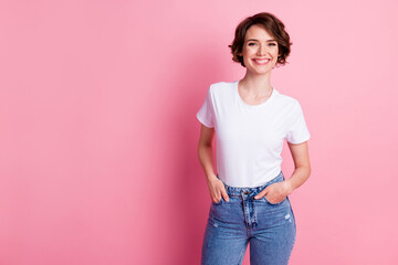 Portrait of attractive cheerful content brown-haired girl holding hands in pockets isolated over pink pastel color background