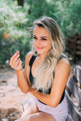 cute girl eats pink grapes sitting on a wooden bench in the woods in the summer in nature