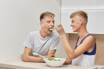Obraz na płótnie Canvas Cute gay couple, LGBT couple, having Breakfast together in the morning in the kitchen. Feed food with a spoon.