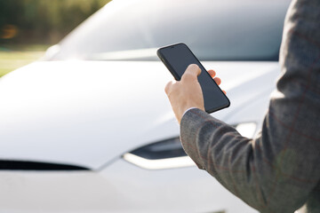 Businessman controls a self-driving electric car using mobile application. Autonomous autopilot driverless car. Smartphone app. Sensor scanning road ahead for vehicles, danger, speed limits.