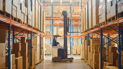 Retail Warehouse full of Shelves with Goods: Electric Forklift Truck Operator Lifting Pallet with Cardboard Box on a Shelf. Working in Logistics Storehouse Product Logistics and Delivery Center