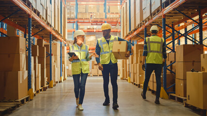 Male and Female Workers Wearing Hard Hats, Have Discussion and Walking Through Retail Warehouse...