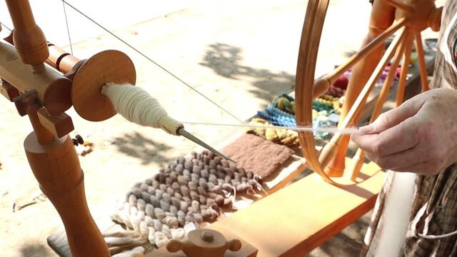 Old hands creating homespun wool yarn on a spinning wheel