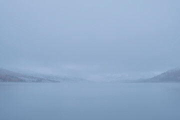 Beautiful mountain lake in autumn during snowfall. Bukhtarminskoe lake in East Kazakhstan. Tourism, travel concept in Kazakhstan. Autumn forest nature. Beautiful fall nature. Outdoor landscape.