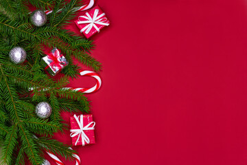 Christmas decorations layout or flatlay with fir branches, gifts, balls and candy canes on red background with copy space.