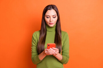 Photo of young beautiful serious calm charming pretty lovely girl use phone chatting isolated on orange color background