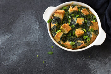 Baked green omelet with spinach and croutons, in white form on dark textured background, flat lay, space
