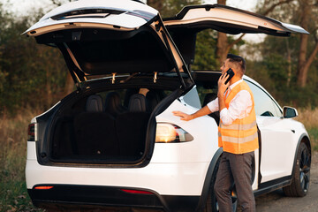 Unhappy businessman speak on phone near the broken electric car help repair stress problem...