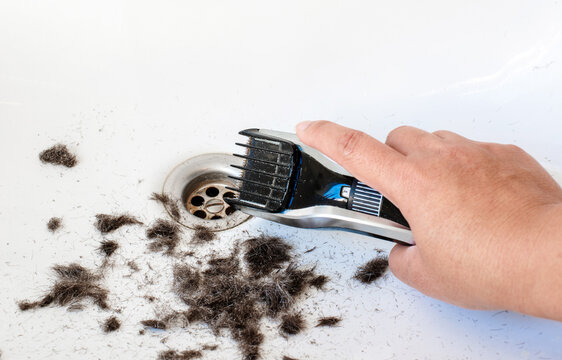 A Hand Holding A Trimmer Over The Sink And A Lot Of Hair In The Background