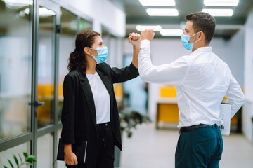 Two manager in protective medical masks bumping elbows while greeting each other in in modern office. Business partners handshake during coronavirus. Covid-19.