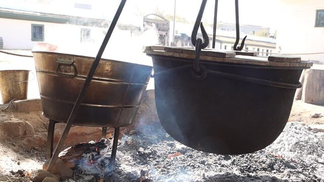 Steam rolls from washpots and steel cauldrons suspended over a wood fire