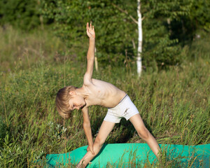 Fototapeta premium Cute boy child practices yoga in Utthita Trikonasana, extended triangle pose. Kids healthy lifestyle, children yoga