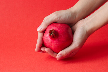 Pomegranate is juicy and bright. Ripe pomegranate is held by women's hands. Fresh, raw fruit on a...