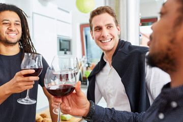 Freunde beim Anstoßen mit Glas Rotwein in der Küche auf Feier