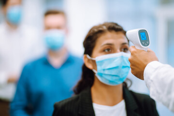 Body Temperature Control. Office staff in protective face masks undergo temperature screening at the entrance. Epidemic virus outbreak concept. COVID-19.