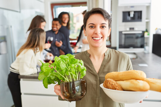 Frau mit Topf Basilikum und Schale Baguette in Küche mit Freunden