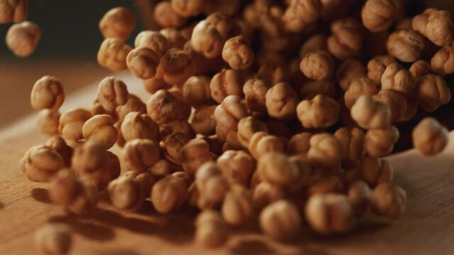 In a beautiful light, Roasted chickpeas fall into the wooden plate. 4K,Very close up, phantom camera,900 fps video.