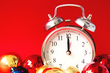 Obraz na płótnie Canvas Beautiful vintage silver alarm clock and set of red, blue and golden Christmas balls on a bright red background. Time concept. Close up. Side view