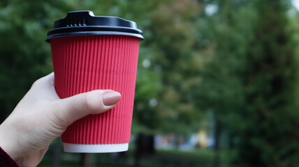 A young girl in a coat holds morning coffee with her while walking in the park. Hand holding paper...